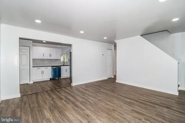 a view of an empty room with wooden floor and a kitchen