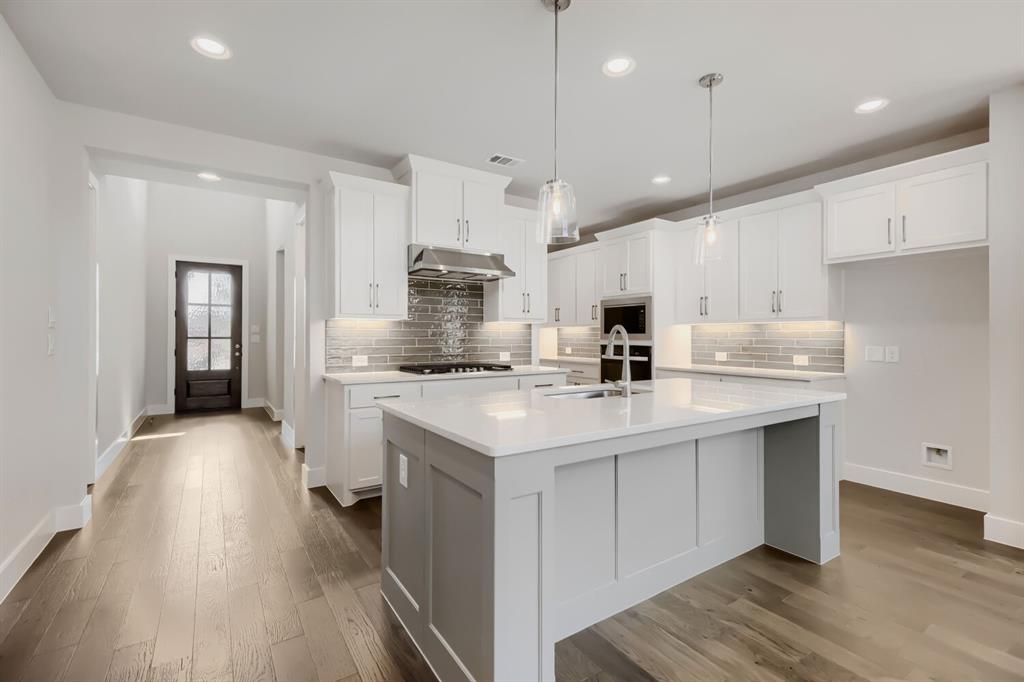 4407 Windy Point Road Oak Point, TX 75068 - Photo 7 of 27 Spacious kitchen featuring an expansive central island with a sink, white cabinetry with under-cabinet lighting, stainless steel appliances, and wood-finish flooring