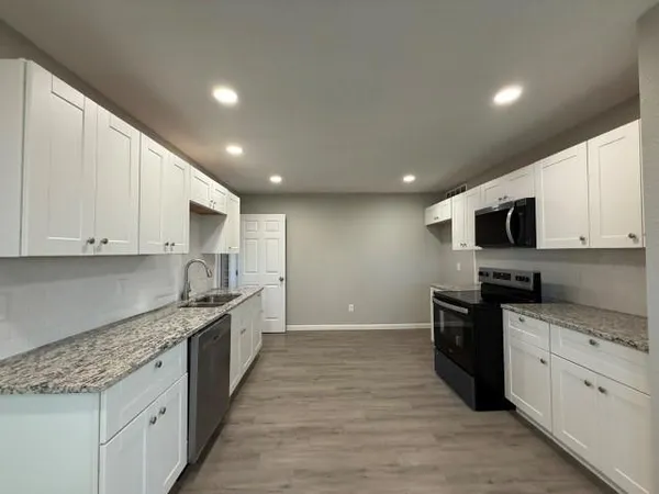 a large kitchen with stainless steel appliances granite countertop a stove top oven a sink dishwasher and a oven with white cabinets