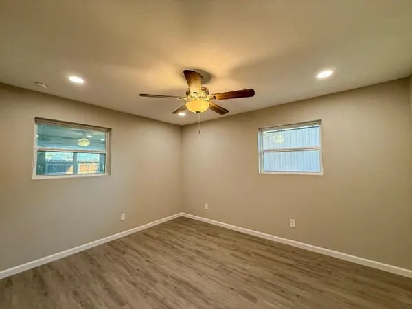 a view of an empty room with wooden floor and a ceiling fan