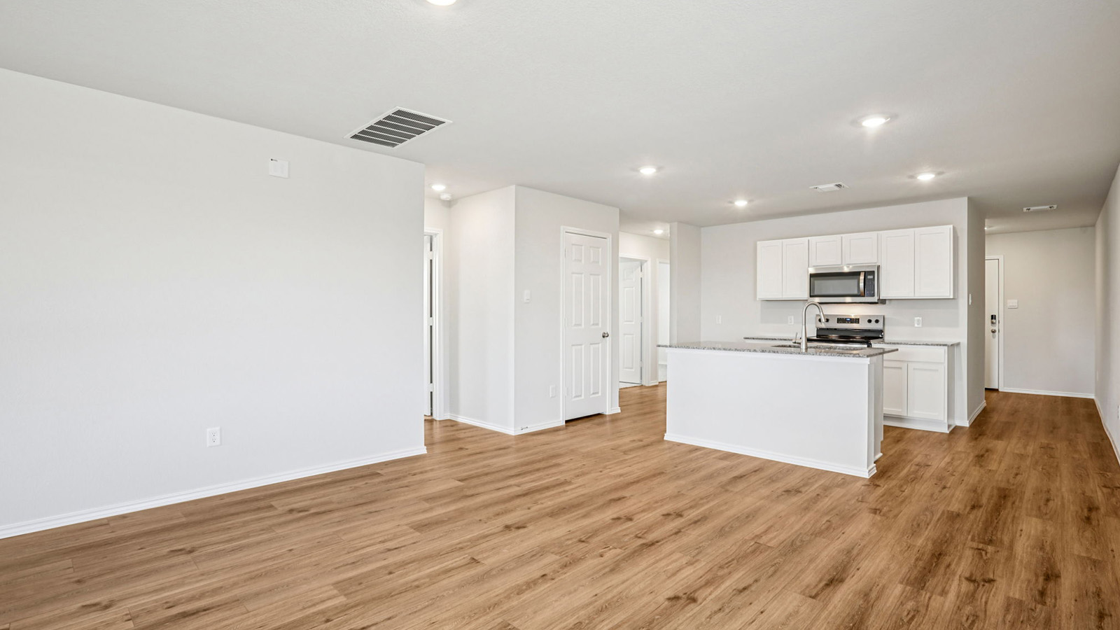148 Wyatt Way Jarrell, TX 76537 - Photo 9 of 33 Open-concept living space featuring wood-finish flooring, recessed lighting, and a kitchen with white cabinetry, granite-style countertops, stainless steel appliances, and an island with an undermount sink