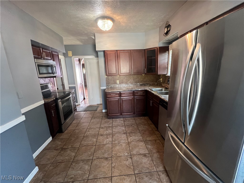 3505 Silsby Road Cleveland, OH 44118 - Photo 6 of 34 Kitchen with appliances with stainless steel finishes, a textured ceiling, glass insert cabinets, baseboards, and decorative backsplash