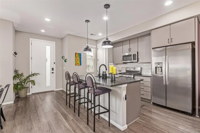 a kitchen with stainless steel appliances a refrigerator a stove a sink dishwasher a dining table and chairs with wooden floor