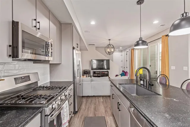 a kitchen with granite countertop a stove a sink a refrigerator wooden floor cabinets and dining table