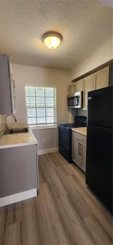 a kitchen with stainless steel appliances granite countertop a sink a stove a refrigerator a washer dryer and a dining table with wooden floor