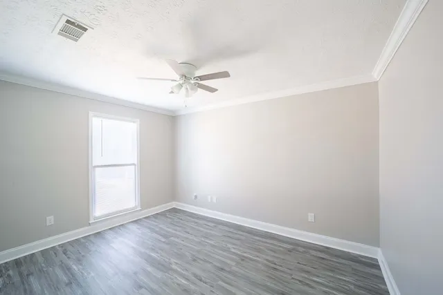an empty room with wooden floor ceiling fan and windows