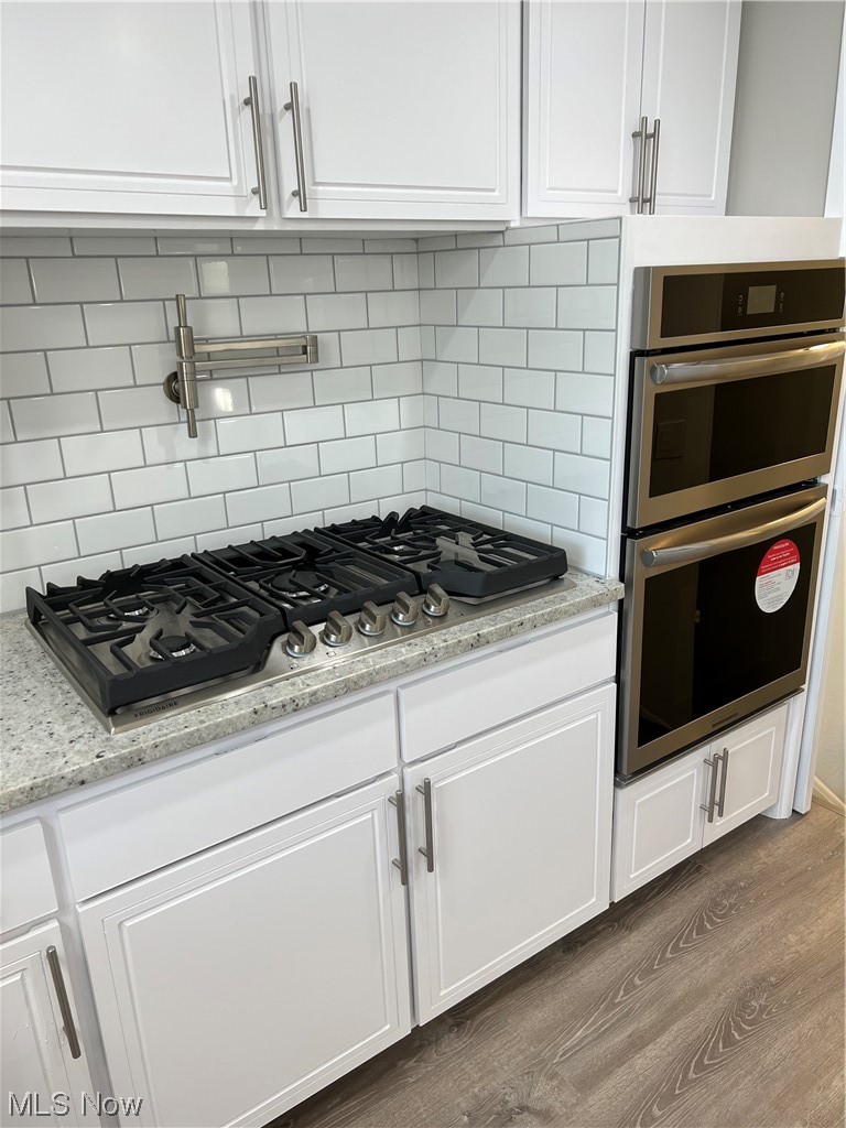 19306 Libby Road Maple Heights, OH 44137 - Photo 6 of 33 Kitchen with dark wood-type flooring, double wall oven, light stone countertops, backsplash, and white cabinetry