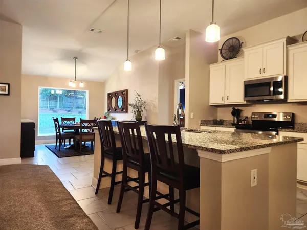 a kitchen with stainless steel appliances granite countertop a stove top oven a sink a dining table and chairs with wooden floor