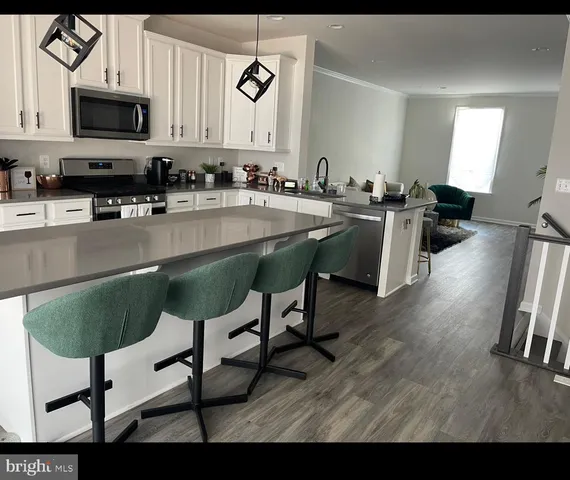 a kitchen with stainless steel appliances granite countertop a stove top oven a sink a dining table and chairs with wooden floor