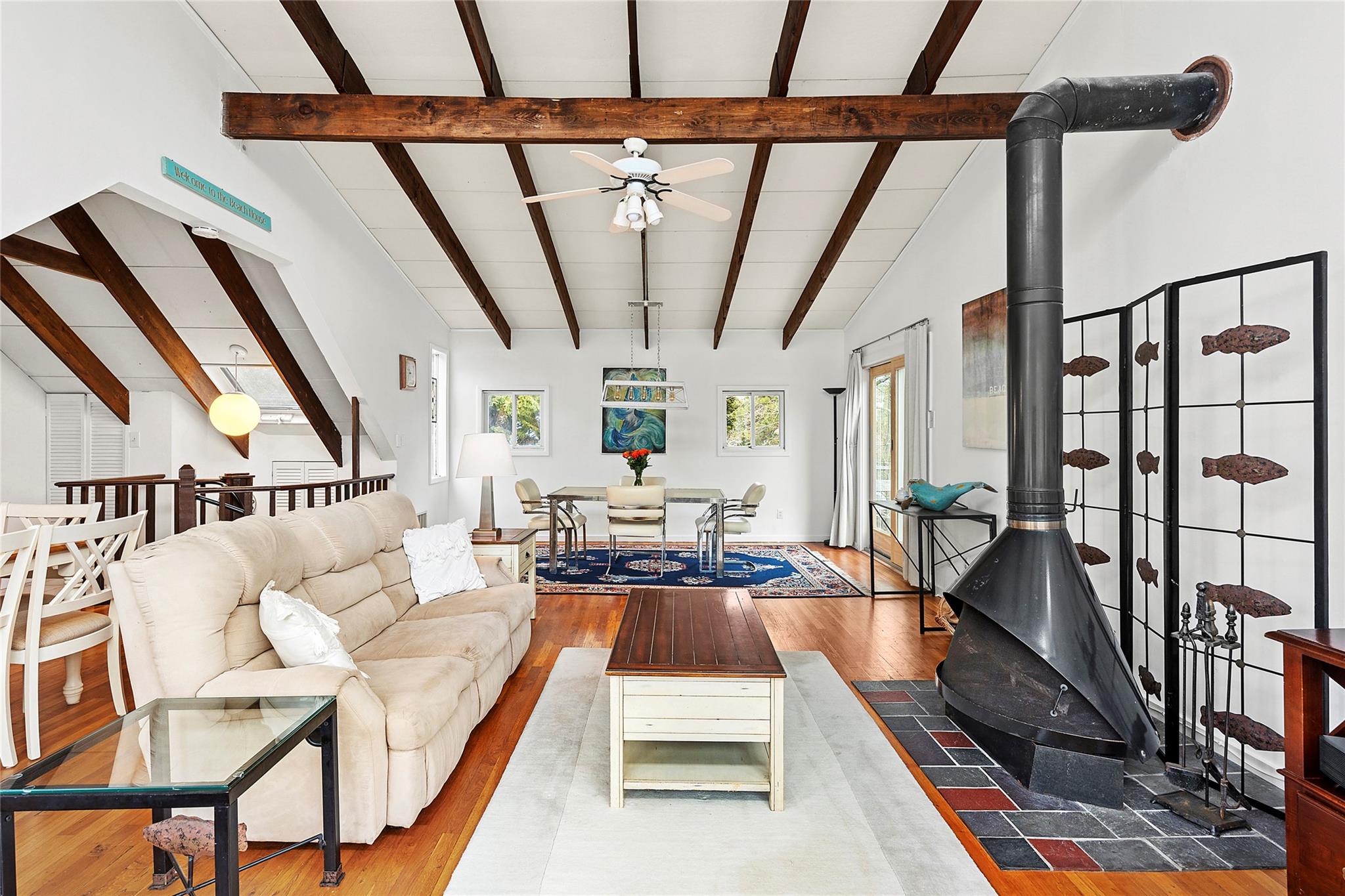 Living area featuring a wood stove, ceiling fan, lofted ceiling with beams, and wood finished floors