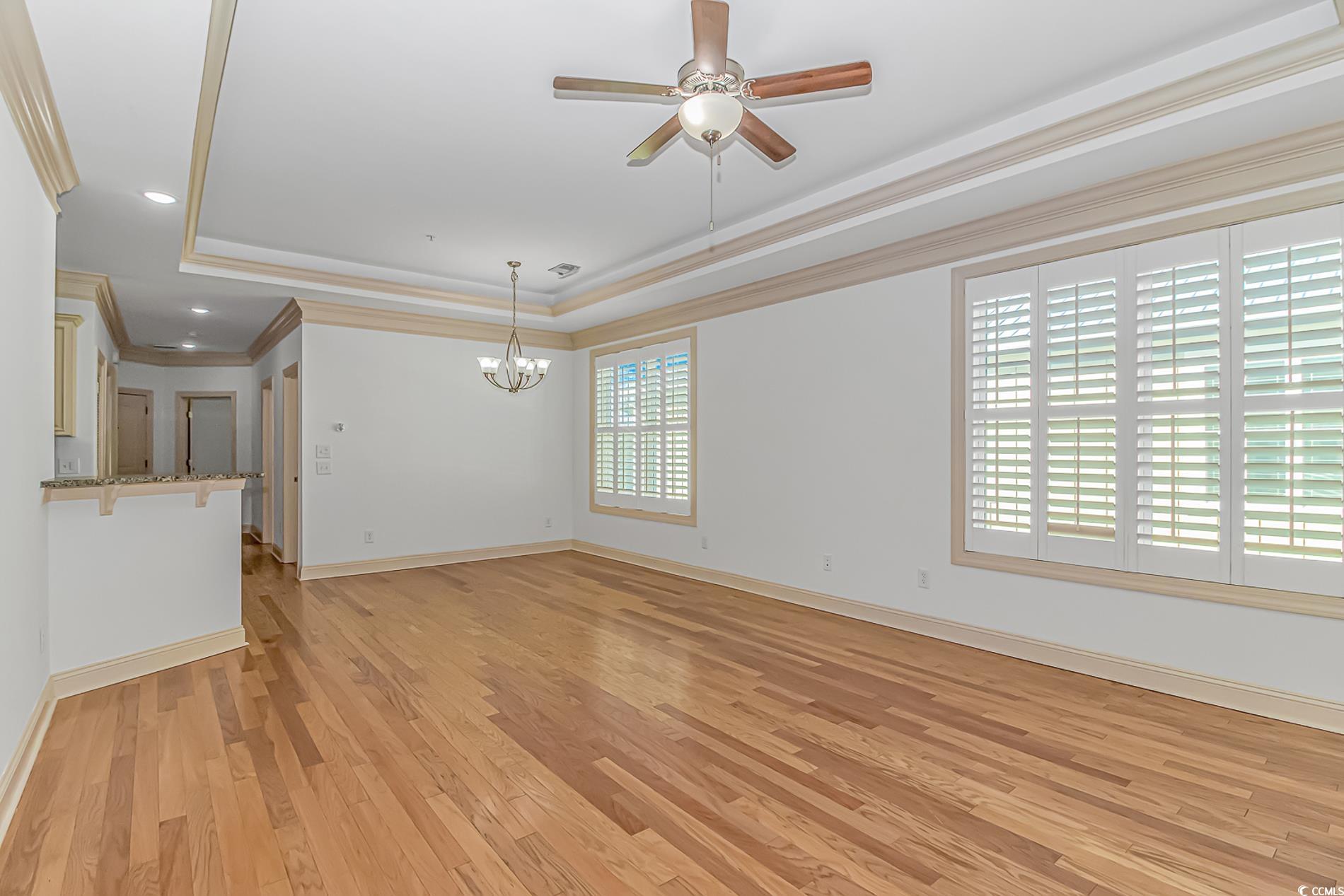 128 Puffin Drive, Unit 3A Pawleys Island, SC 29585 - Photo 21 of 30 living room featuring crown molding, a raised ceiling, light wood-style floors, a chandelier, and ceiling fan