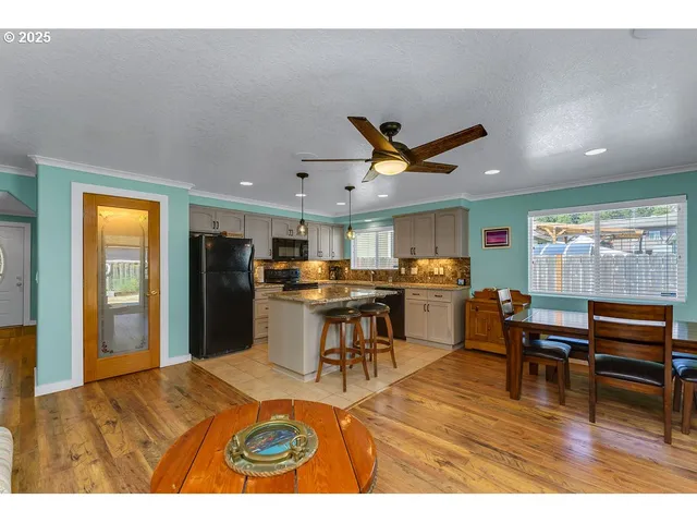 a open kitchen with stainless steel appliances granite countertop a refrigerator a stove a sink a dining table and chairs with wooden floor