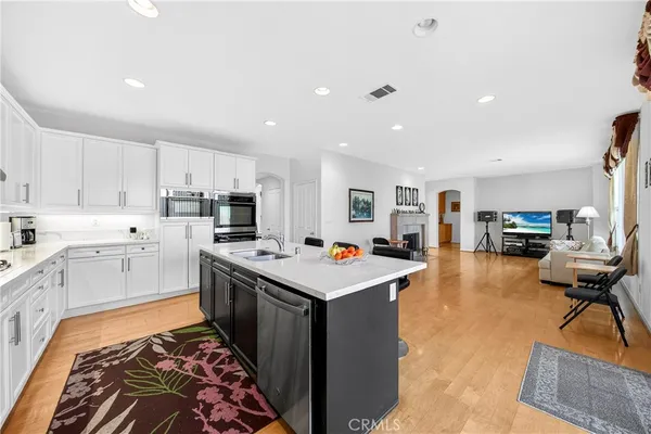 a open kitchen with stainless steel appliances granite countertop a refrigerator oven a sink dishwasher and white cabinets with wooden floor