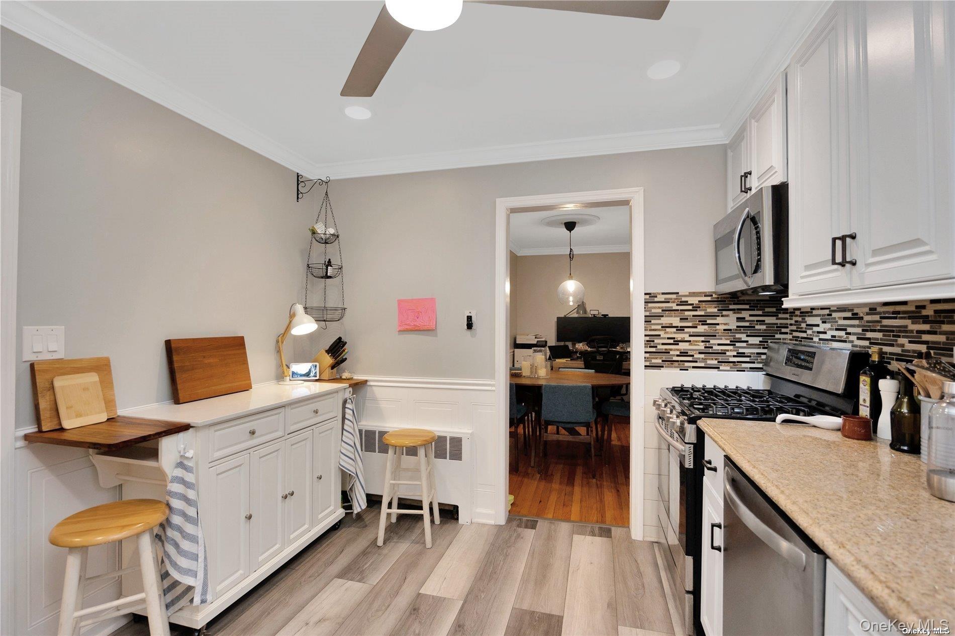 245 West Chester Street Long Beach, NY 11561 - Photo 22 of 31 Kitchen with wainscoting, stainless steel appliances, white cabinetry, crown molding, and light wood-style flooring