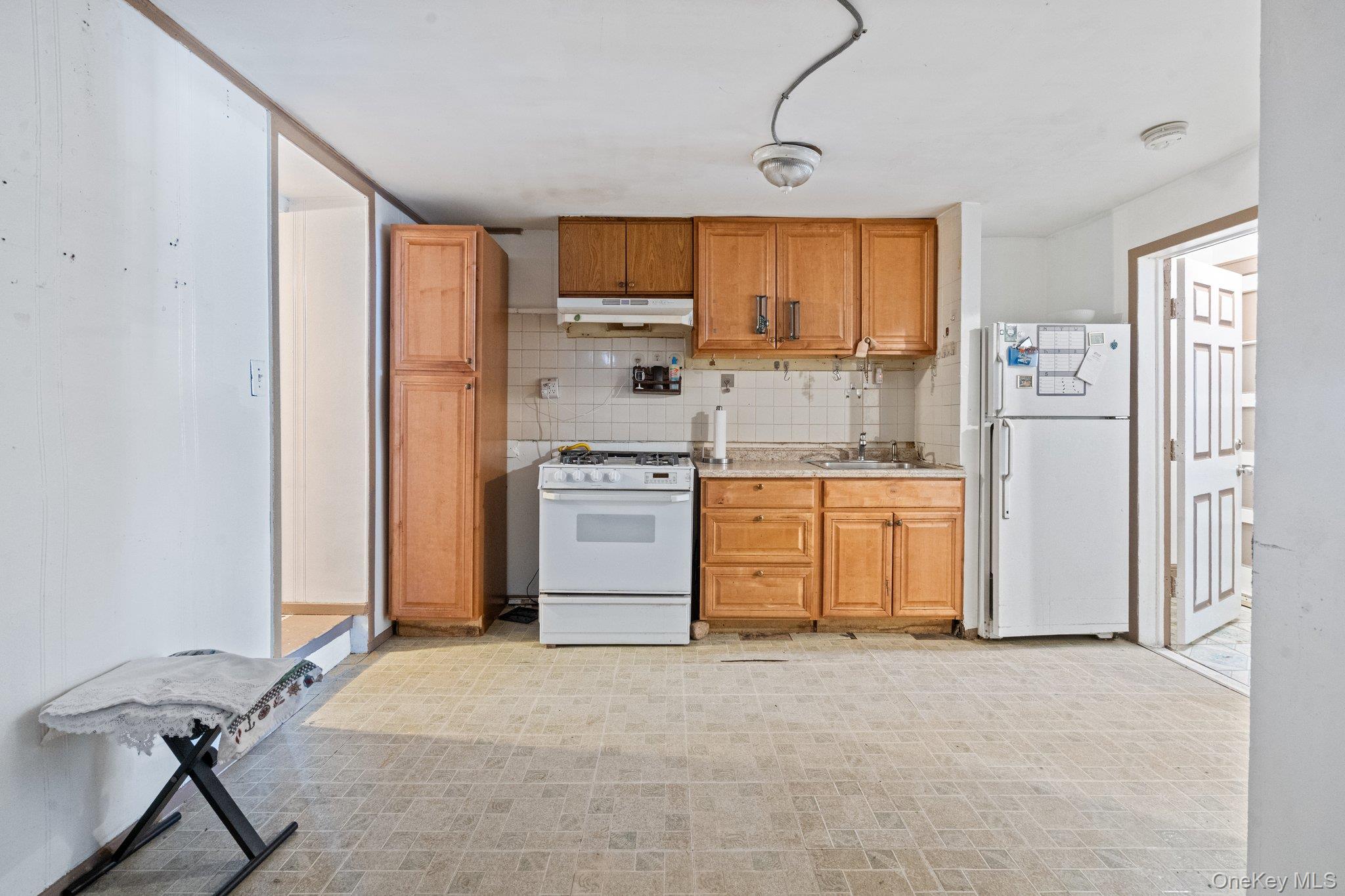 100-30 Martense Avenue Queens, NY 11368 - Photo 13 of 36 Kitchen with white appliances, light countertops, under cabinet range hood, brown cabinets, and backsplash