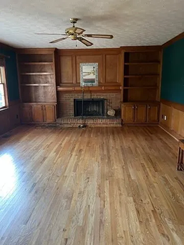 a view of a livingroom with a fireplace a ceiling fan and wooden floor