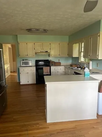 a kitchen with stainless steel appliances granite countertop a stove a sink a refrigerator a microwave oven with white cabinets and wooden floor