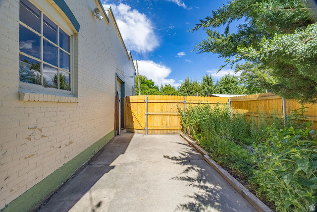 299 West Center Street, Unit 2 Logan, UT 84321 - Photo 32 of 46 Paved exterior pathway featuring a vibrant wooden fence, a brick building with a large window, a side access door, and established greenery