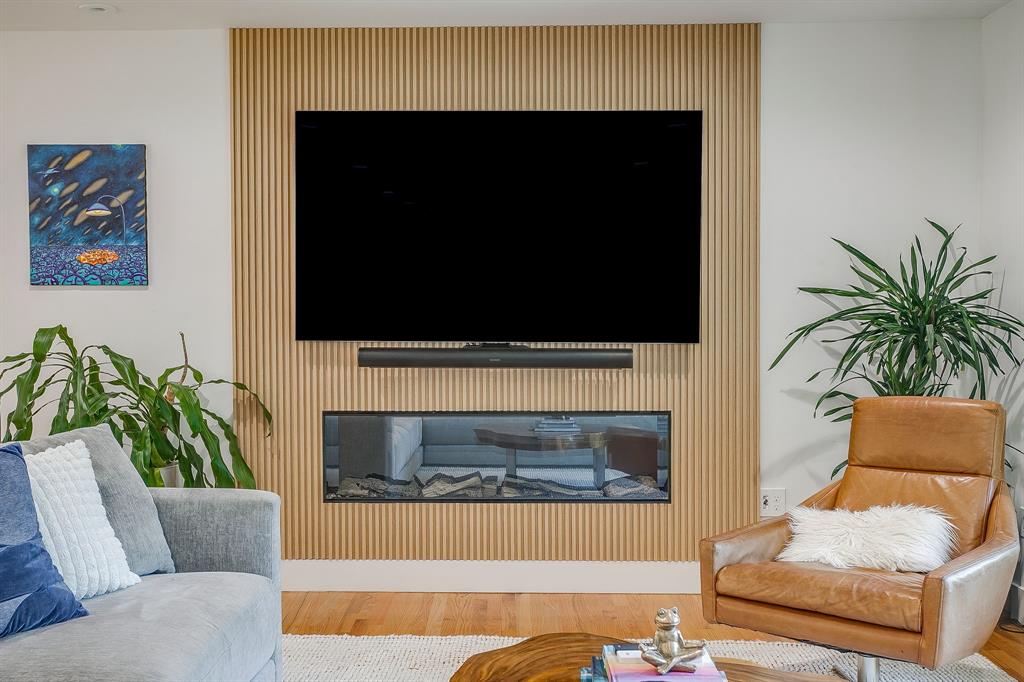 6700 Fortune Road Fort Worth, TX 76116 - Photo 17 of 40 Integrated media wall featuring a slatted wood-finish panel, a built-in linear electric fireplace, and hardwood flooring