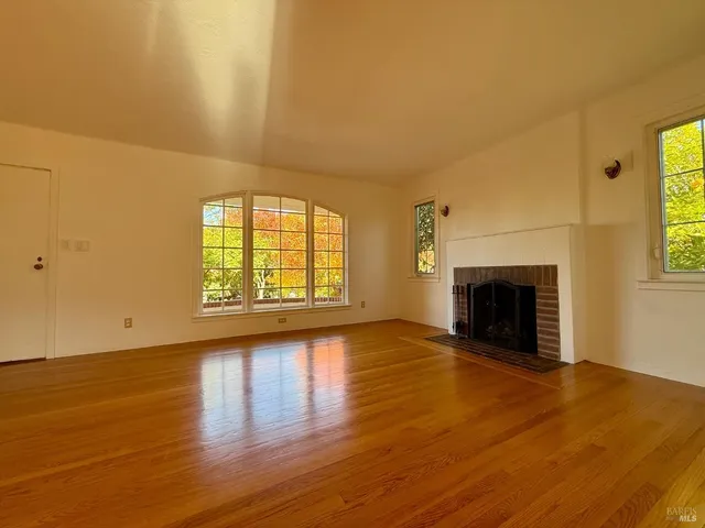 an empty room with wooden floor fireplace and windows