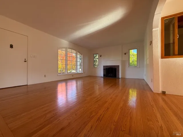an empty room with wooden floor fireplace and windows