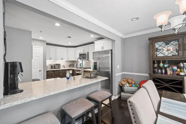 a kitchen with stainless steel appliances kitchen island granite countertop a dining table chairs and a refrigerator