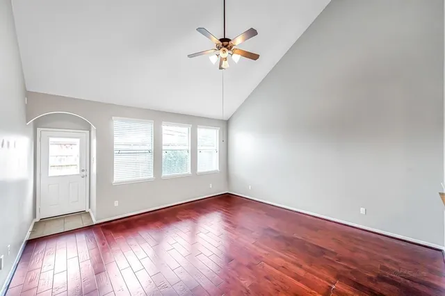 an empty room with wooden floor chandelier fan and windows