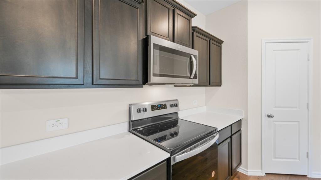 657 Glee Stem Road Lavon, TX 75166 - Photo 5 of 26 Kitchen featuring dark wood cabinetry, white countertops, stainless steel microwave, electric range, and a white paneled door
