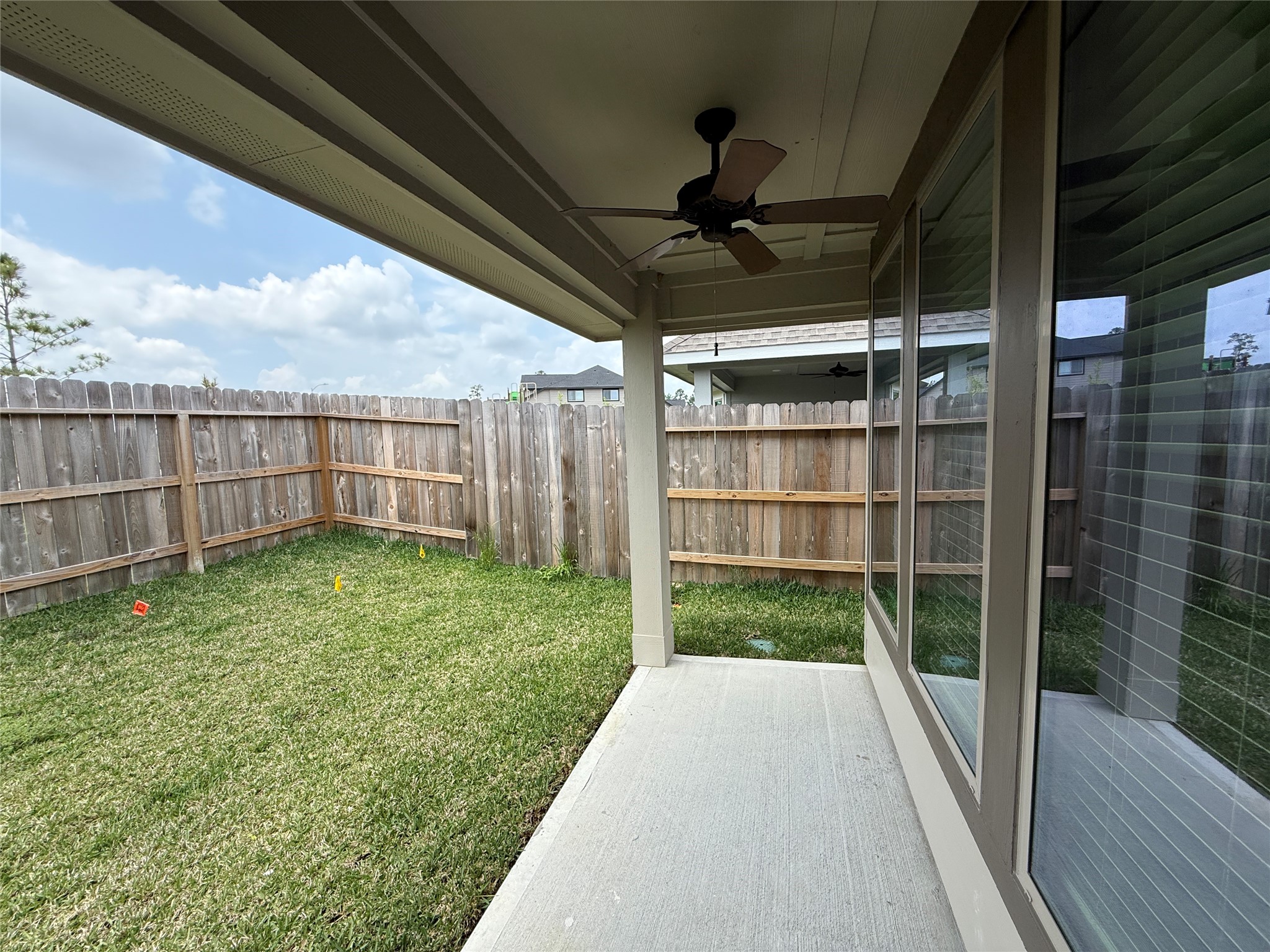 31961 Retama Rnch Drive Spring, TX 77386 - Photo 24 of 25 This photo shows a covered patio with a ceiling fan, overlooking a fenced backyard with a small lawn, ideal for outdoor relaxation and privacy.