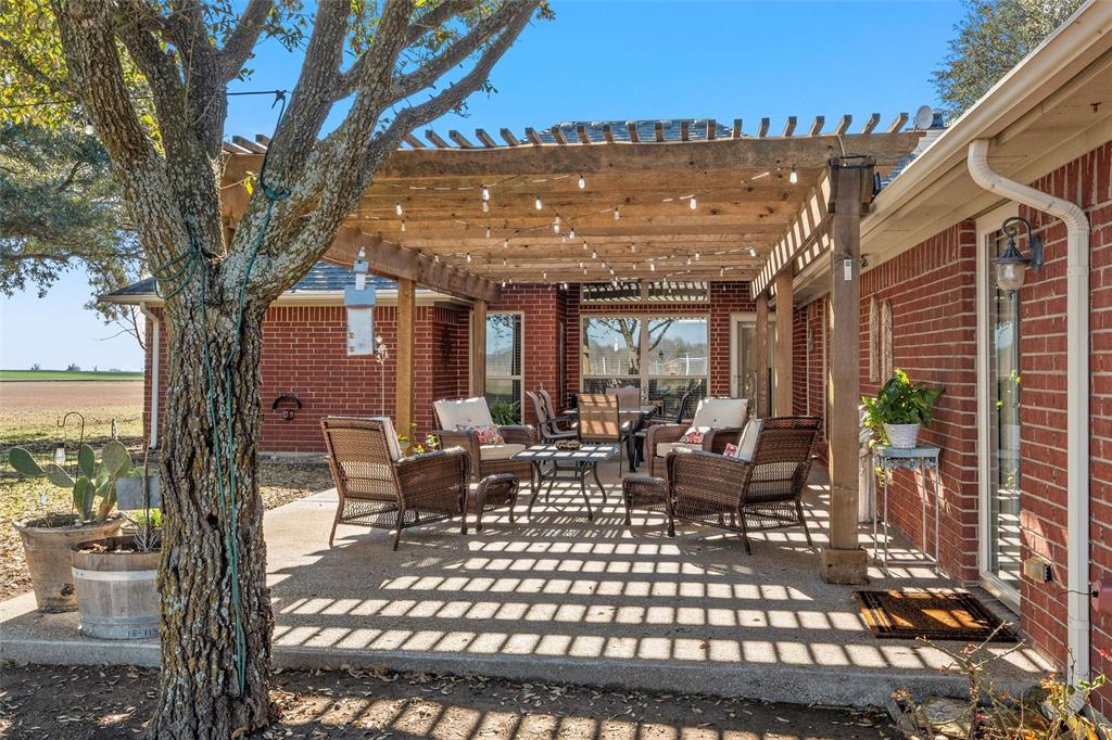 231 Trlica Road West, TX 76691 - Photo 28 of 36 A covered patio with a charming pergola provides a welcoming outdoor living space ideal for relaxing or entertaining, with plenty of room for seating and potted plants. Multiple rear entry points offer convenient access to the home