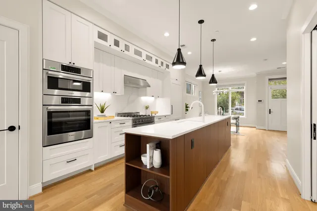 a large white kitchen with kitchen island a stove a sink a refrigerator and white cabinets with wooden floor
