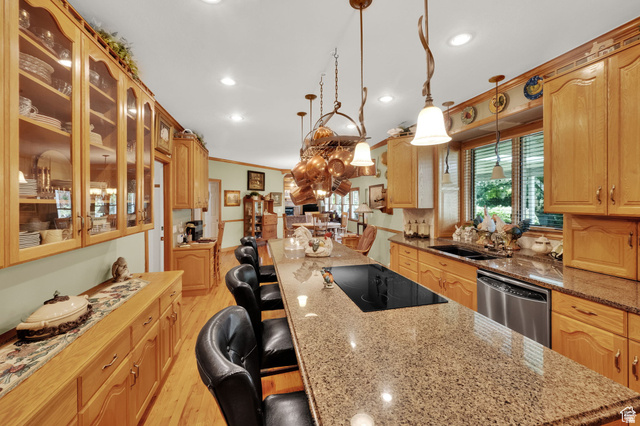7740 Keswick Road Sandy, UT 84093 - Photo 19 of 74 Spacious kitchen featuring a large central island with integrated cooktop, granite countertops, wood-finish flooring, abundant wood cabinetry, and a stainless steel dishwasher