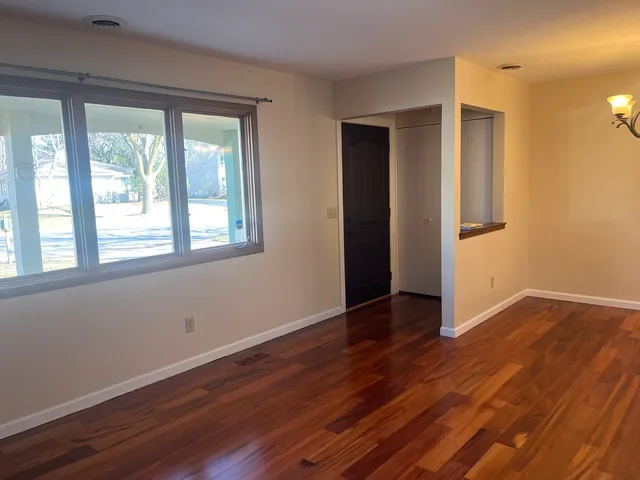 a view of an empty room with wooden floor and a window