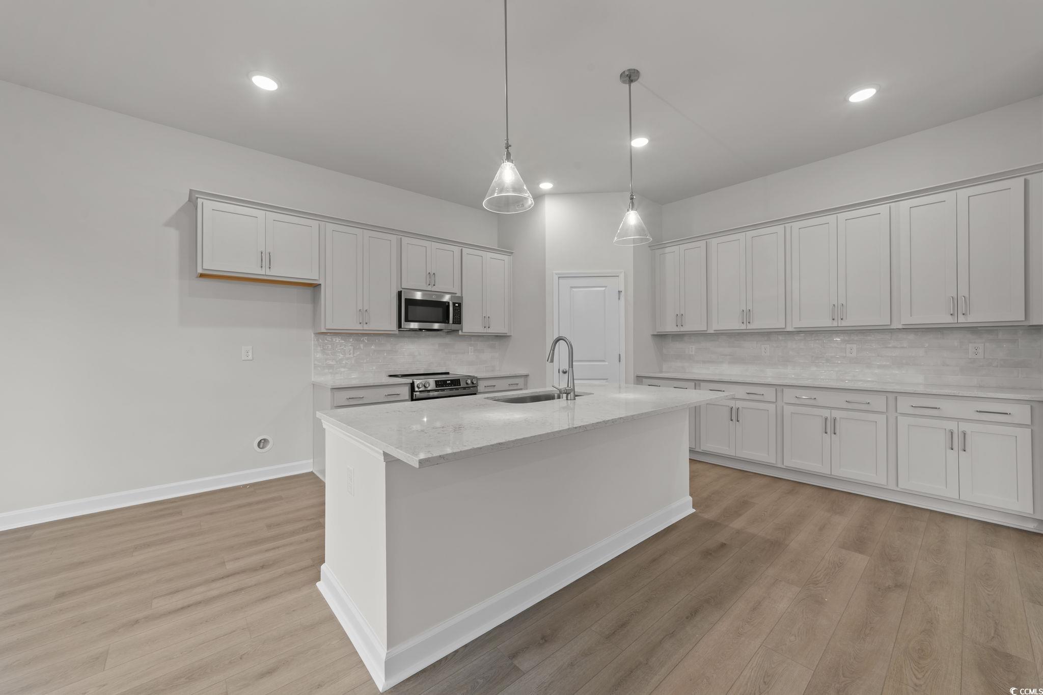 787 Ebb Tide Road Little River, SC 29566 - Photo 12 of 32 Kitchen with hanging light fixtures, light stone countertops, a kitchen island with sink, light wood-style flooring, and stainless steel appliances