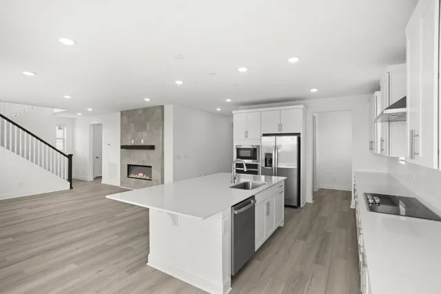 a kitchen with stainless steel appliances a stove top oven a refrigerator a sink and white cabinets with wooden floor