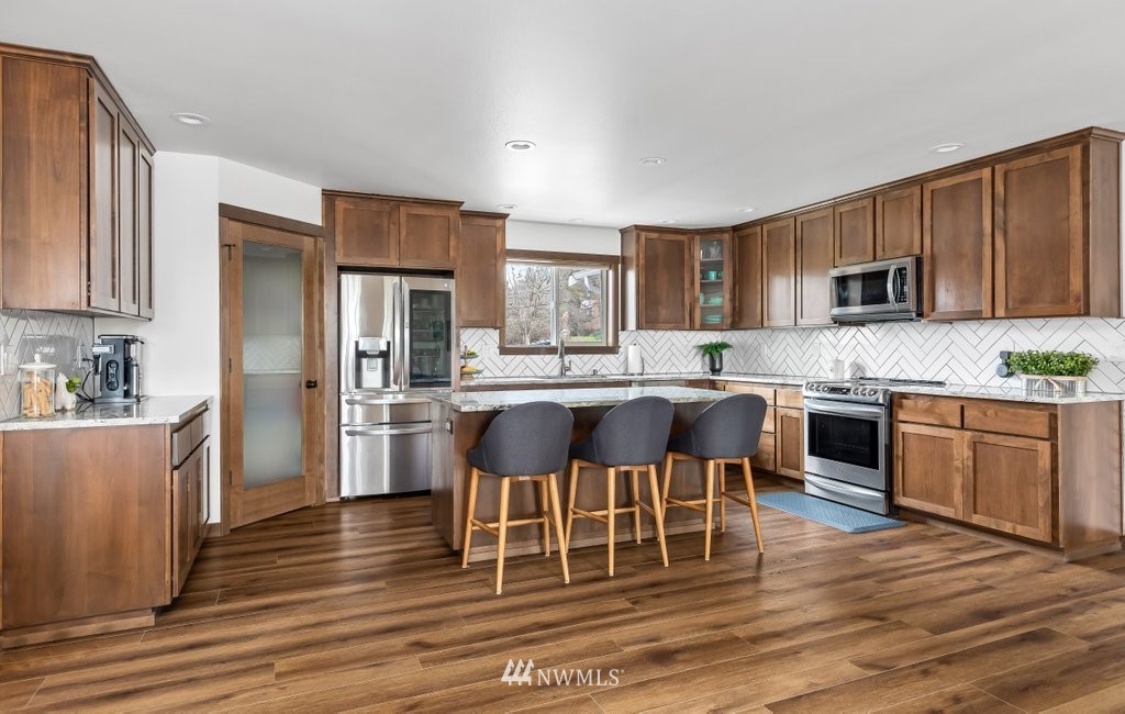 1471 North View Road Oak Harbor, WA 98277 - Photo 5 of 38 a large kitchen with kitchen island granite countertop a stove a sink a refrigerator and white cabinets with wooden floor