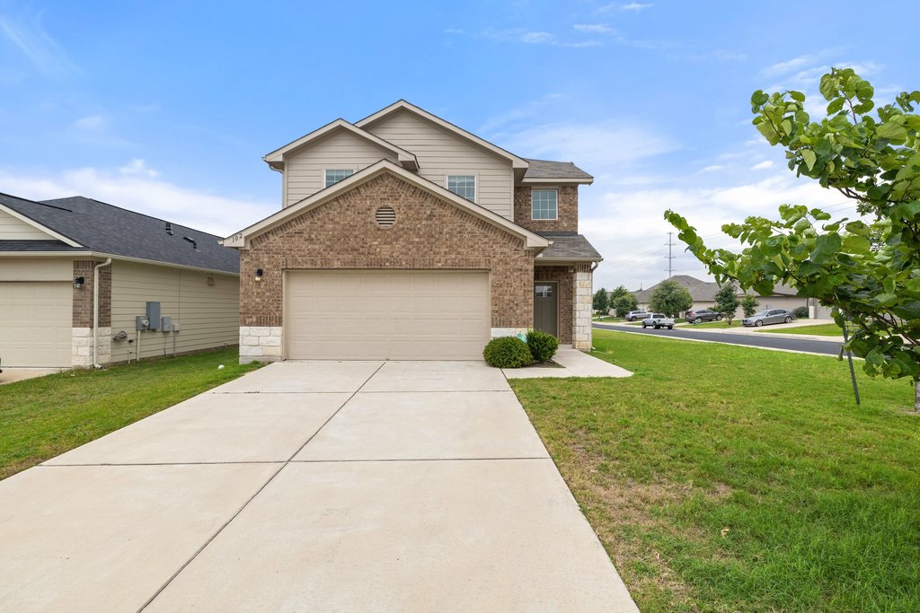 A classic brick and siding two-story home with an attached garage and neatly kept front yard.