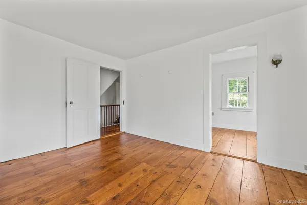 an empty room with wooden floor and way to kitchen