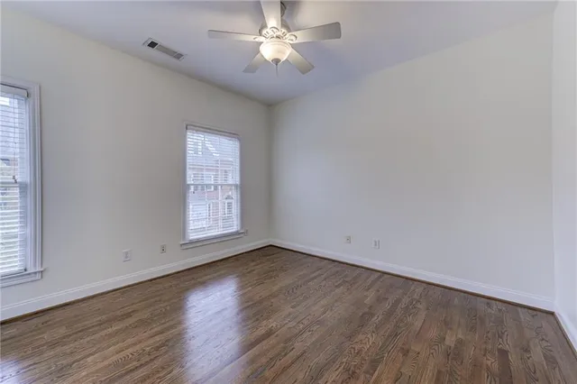 a view of an empty room with wooden floor and a ceiling fan