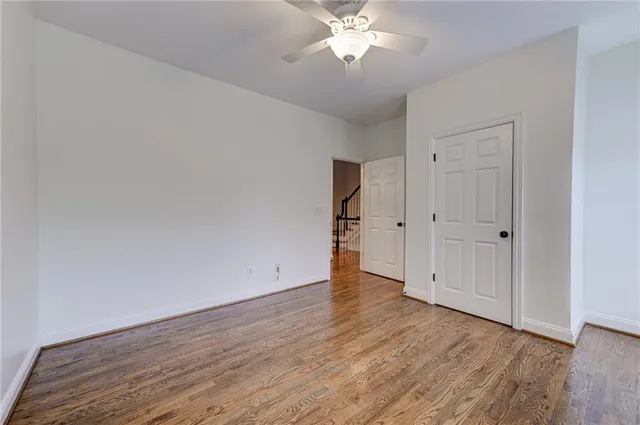 a view of an empty room with wooden floor and a ceiling fan