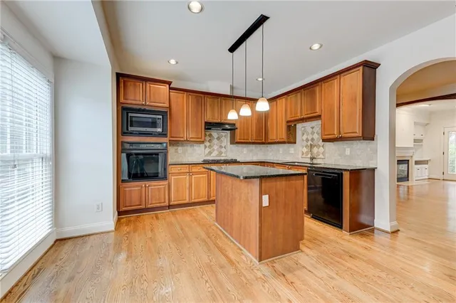 a room with kitchen island granite countertop wooden floor a large window a sink and stainless steel appliances