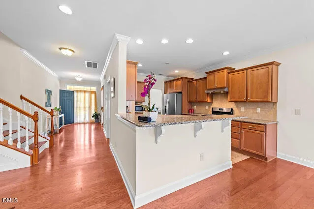 a kitchen with stainless steel appliances kitchen island granite countertop a refrigerator a stove top oven and a sink with cabinets