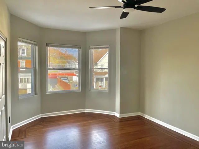 an empty room with wooden floor fan and windows