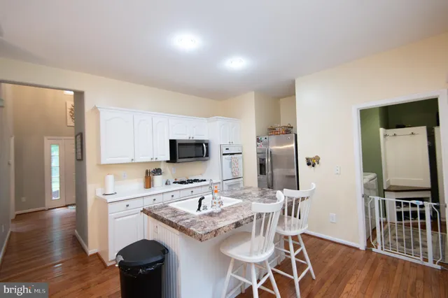 a kitchen with stainless steel appliances kitchen island granite countertop a sink dishwasher a refrigerator and a stove with wooden floor