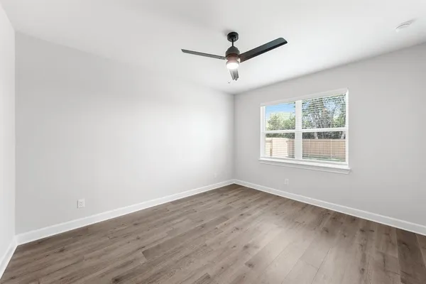 an empty room with wooden floor ceiling fan and window