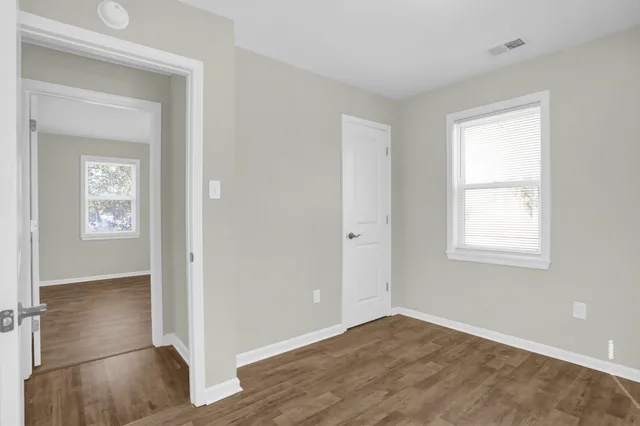 an empty room with wooden floor closet and windows
