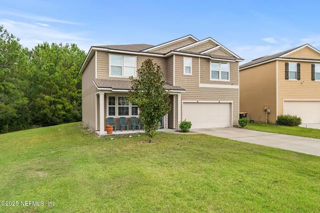 a view of a yard in front of a house with plants and large tree
