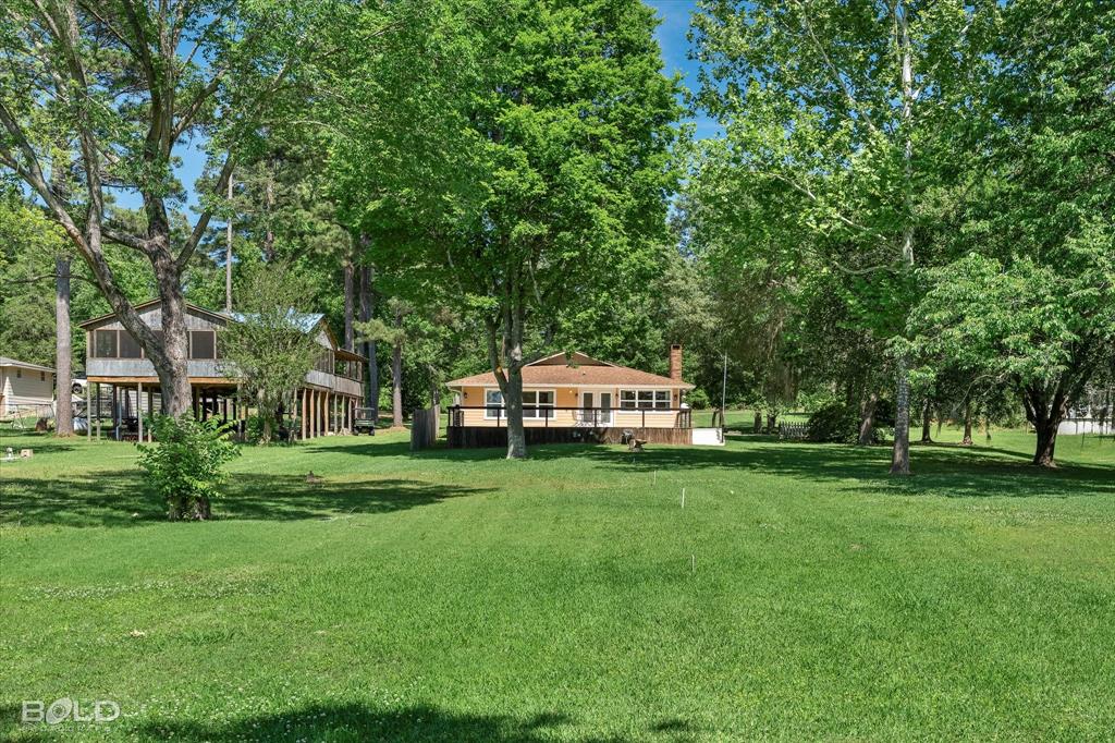 225 Marie Road Ringgold, LA 71068 - Photo 15 of 40 Spacious green lawn surrounded by mature trees, featuring a raised residence with a full-width deck and a visible chimney