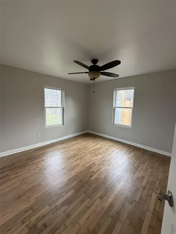 an empty room with wooden floor fan and windows