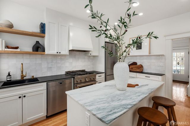 a kitchen with stainless steel appliances granite countertop a sink a stove white cabinets and wooden floor